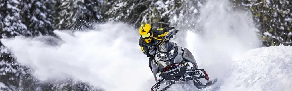 Райдер на снегоходе Ski-Doo Renegade X-RS поднимает облако снега в лесу